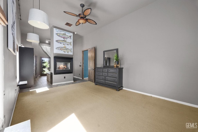 unfurnished bedroom featuring a high ceiling, a multi sided fireplace, baseboards, visible vents, and carpet