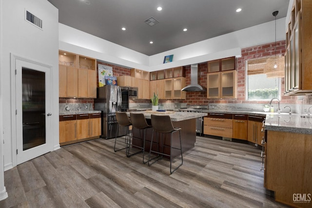 kitchen with visible vents, wood finished floors, stainless steel appliances, a sink, and wall chimney range hood