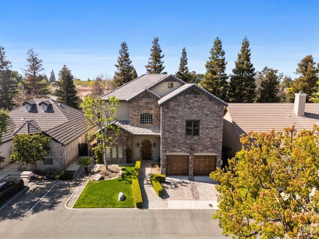 traditional home with stone siding, a tile roof, decorative driveway, and an attached garage