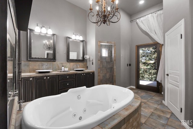 full bath featuring decorative backsplash, a tub with jets, a sink, double vanity, and a notable chandelier
