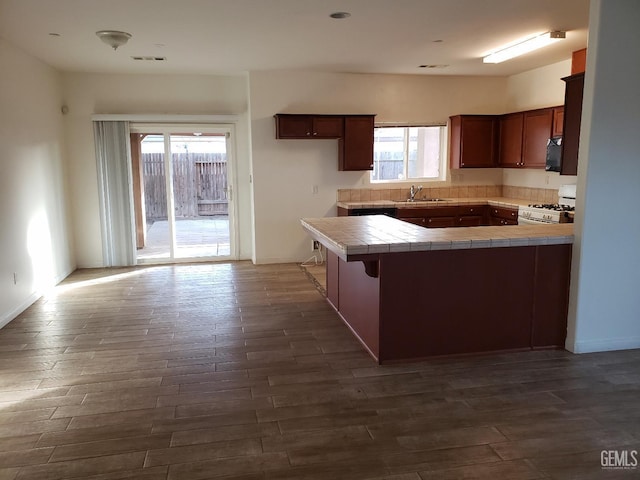 kitchen with kitchen peninsula, white range with gas cooktop, sink, dark hardwood / wood-style floors, and tile counters