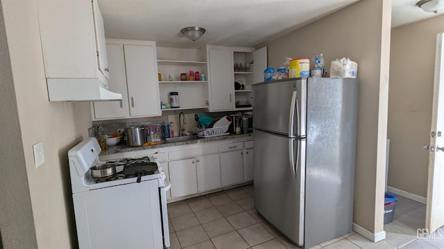 kitchen with sink, light tile patterned floors, stainless steel fridge, white gas range oven, and white cabinets