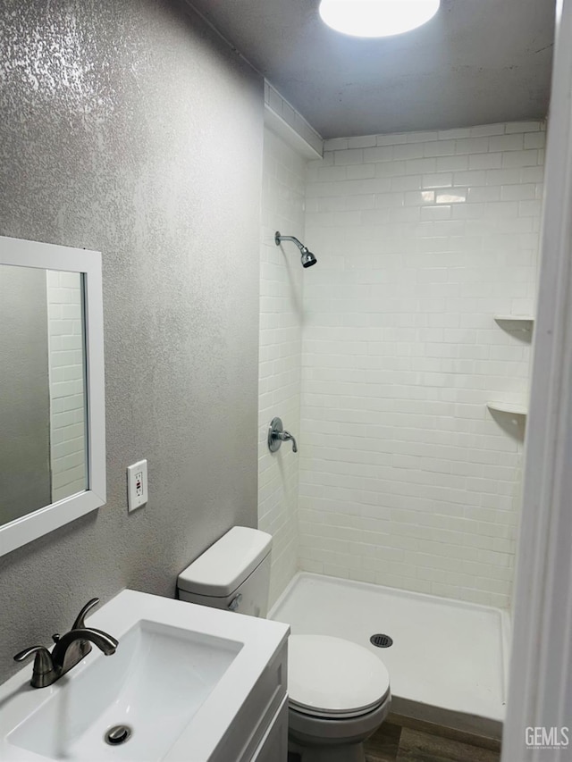 bathroom with a tile shower, vanity, and toilet