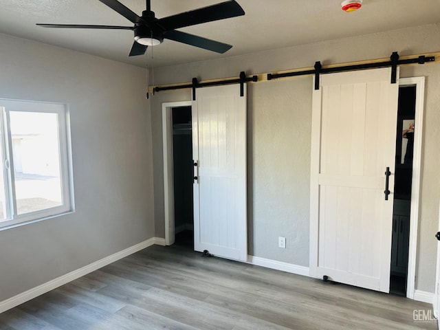 unfurnished bedroom featuring ceiling fan, a barn door, and light hardwood / wood-style floors