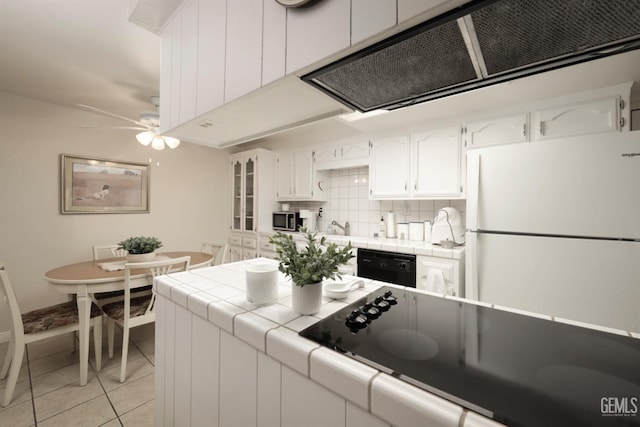 kitchen with tile countertops, black appliances, light tile patterned floors, tasteful backsplash, and white cabinetry