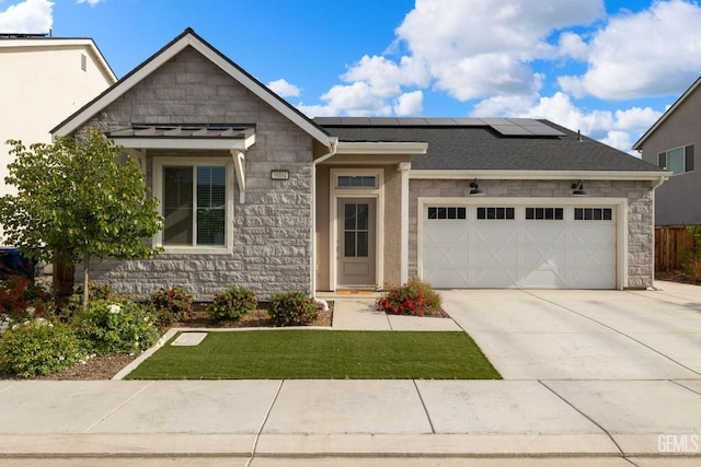 view of front of property featuring stone siding, solar panels, a garage, and driveway