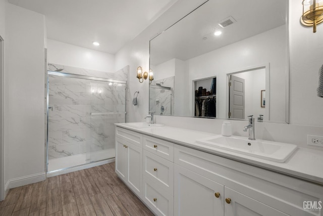 bathroom featuring a marble finish shower, double vanity, wood finished floors, and a walk in closet