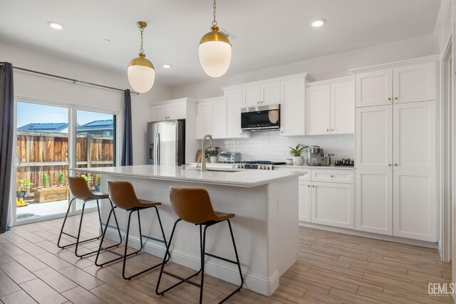 kitchen featuring stainless steel appliances, a sink, a kitchen island with sink, decorative backsplash, and a breakfast bar area
