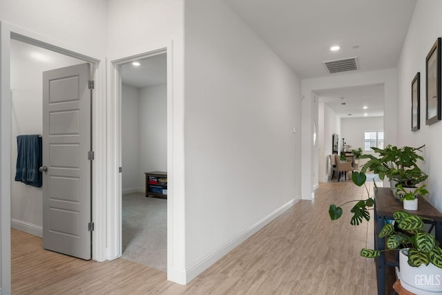 hallway featuring light wood-style floors, baseboards, and recessed lighting