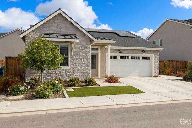 view of front of house with stone siding, solar panels, fence, and an attached garage