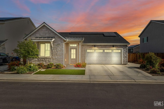 view of front of home featuring stone siding, driveway, solar panels, a garage, and a standing seam roof