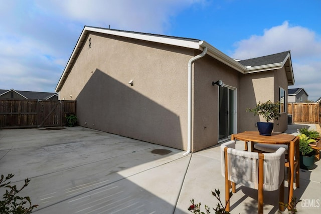 rear view of house featuring a patio area, stucco siding, fence, and a gate