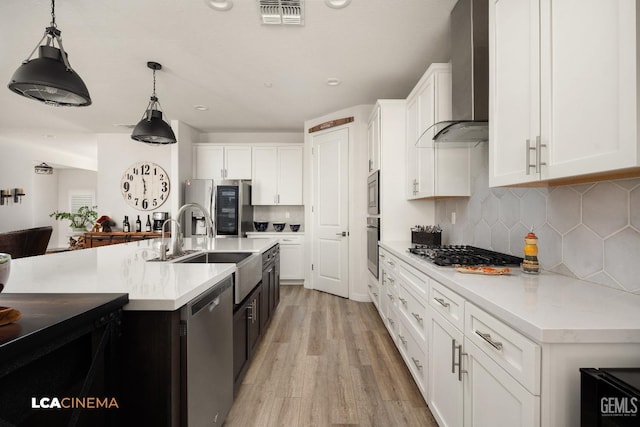 kitchen with decorative backsplash, wall chimney exhaust hood, stainless steel appliances, decorative light fixtures, and white cabinets