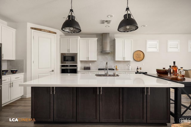 kitchen featuring wall chimney exhaust hood, a large island with sink, appliances with stainless steel finishes, and tasteful backsplash