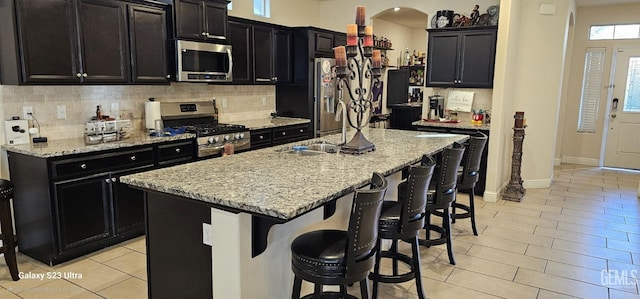 9211 Woodbrook Dr, Shafter, CA 93263 - kitchen with dark cabinetry, a breakfast bar, arched walkways, stainless steel appliances, and an island with sink