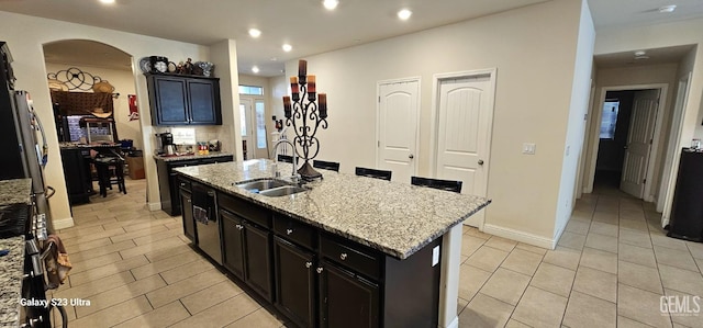 9211 Woodbrook Dr, Shafter, CA 93263 - kitchen featuring a sink, light stone counters, an island with sink, arched walkways, and dark cabinetry