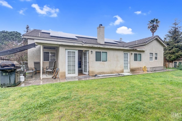 rear view of property featuring a lawn, solar panels, a patio, and stucco siding