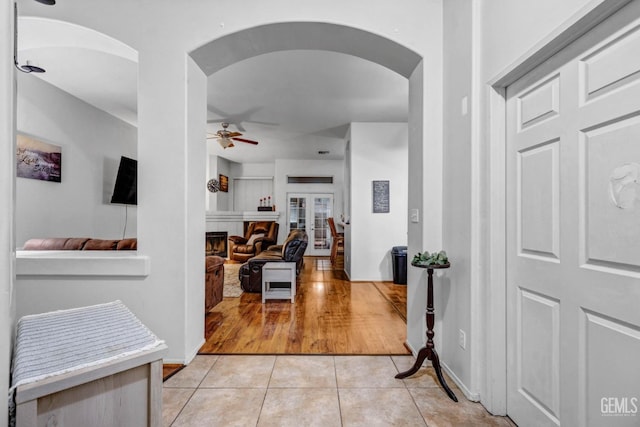 entrance foyer featuring baseboards, ceiling fan, light tile patterned floors, a fireplace, and arched walkways