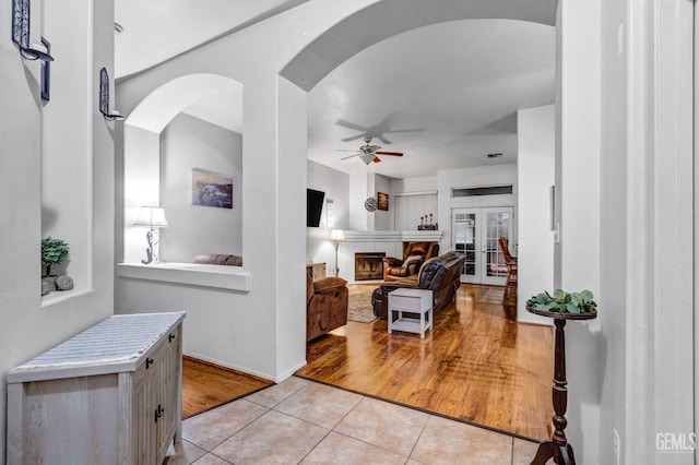 living room featuring a ceiling fan, french doors, arched walkways, light tile patterned floors, and a tile fireplace