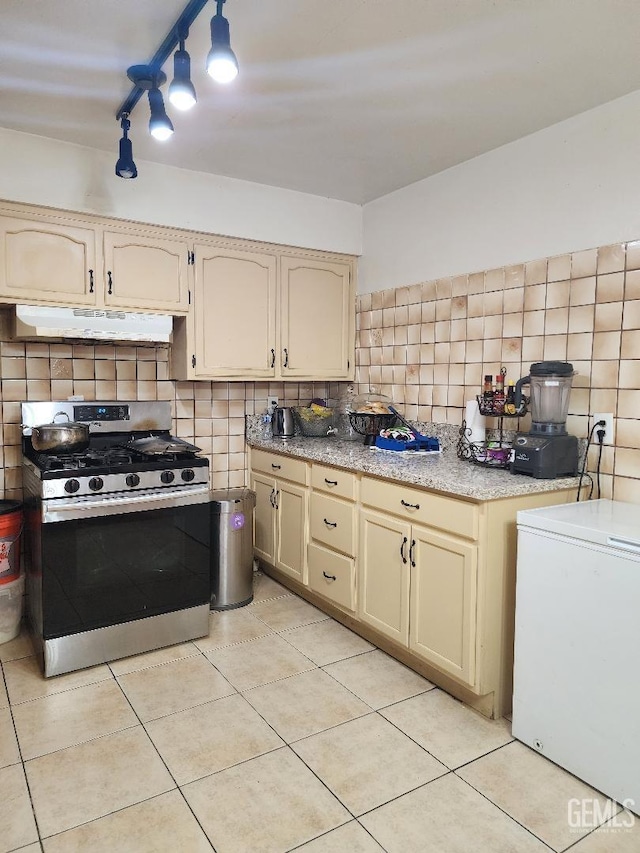 kitchen with fridge, cream cabinetry, light tile patterned floors, backsplash, and gas stove