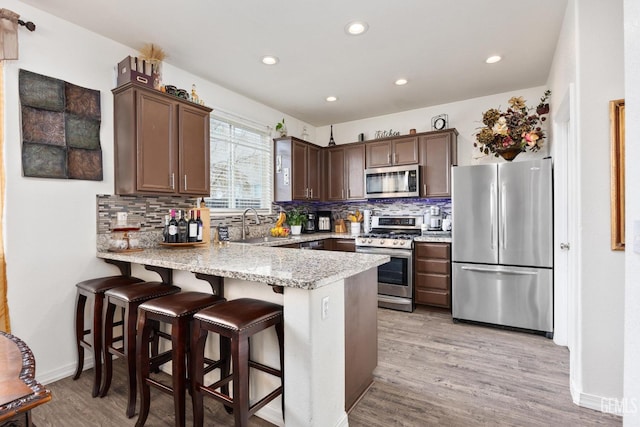 kitchen with sink, a breakfast bar area, kitchen peninsula, stainless steel appliances, and light hardwood / wood-style floors