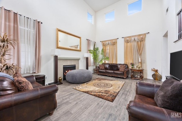 living room featuring a tile fireplace, a towering ceiling, and light hardwood / wood-style flooring