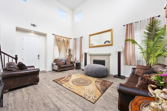 living room with a tile fireplace, a towering ceiling, and light wood-type flooring