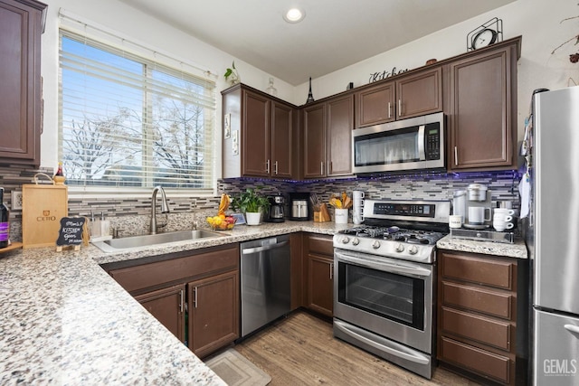 kitchen featuring sink, appliances with stainless steel finishes, backsplash, light stone countertops, and light hardwood / wood-style floors