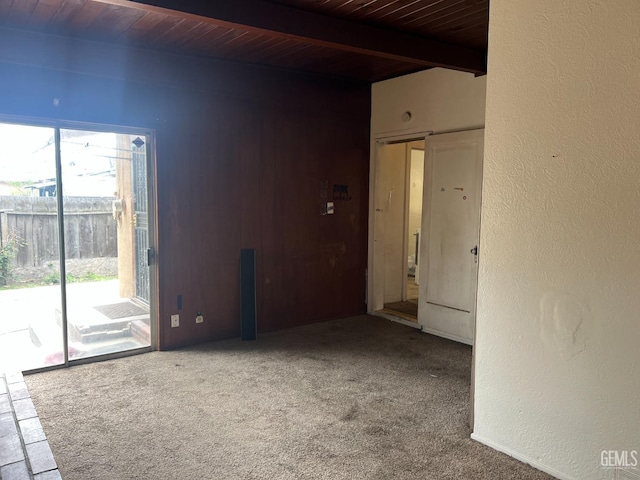 empty room with beam ceiling, carpet flooring, a textured wall, and wooden ceiling