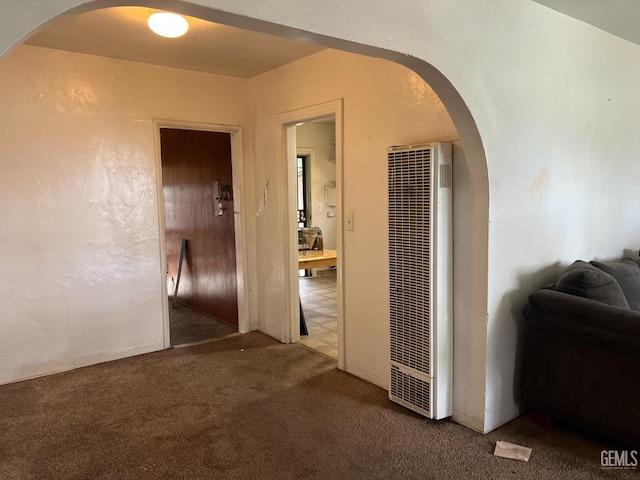 corridor featuring arched walkways, carpet, a heating unit, and a textured wall