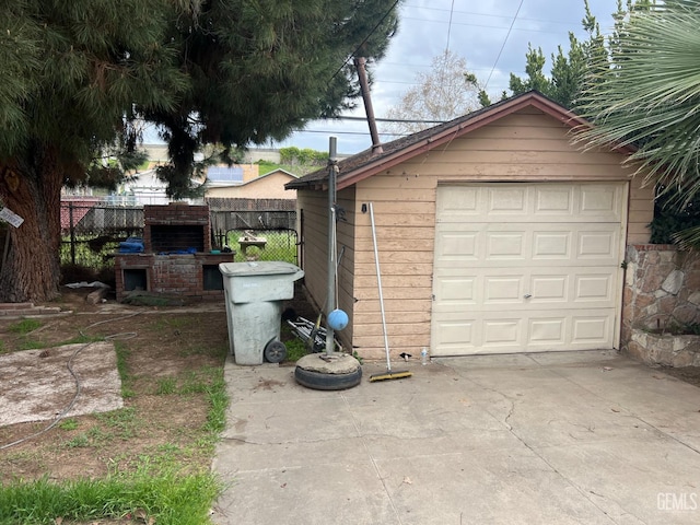 detached garage featuring exterior fireplace, concrete driveway, and fence