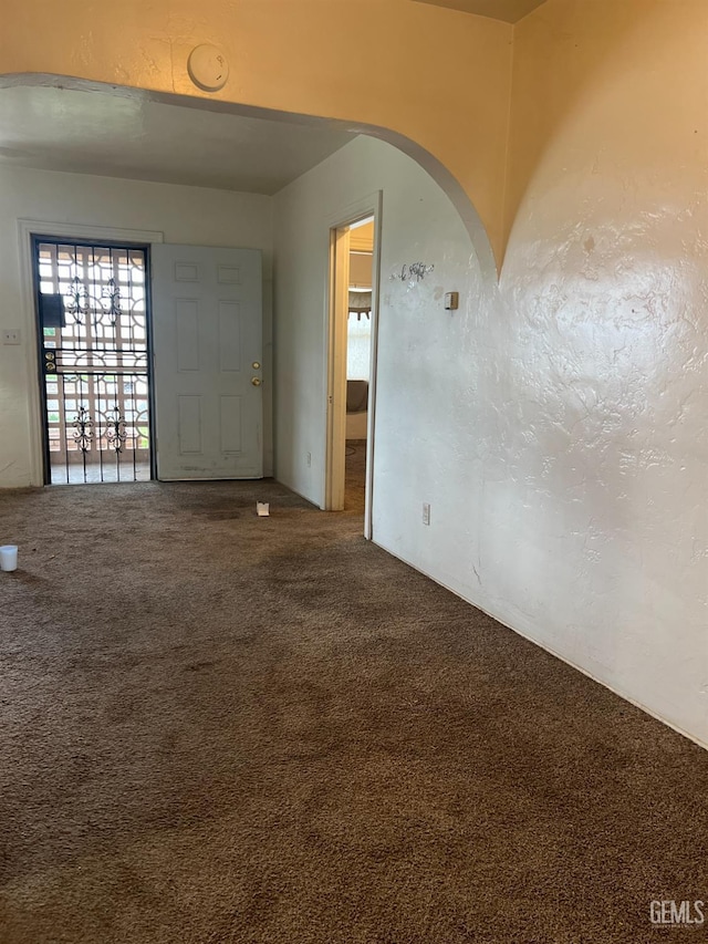 entryway featuring arched walkways, carpet, and a textured wall