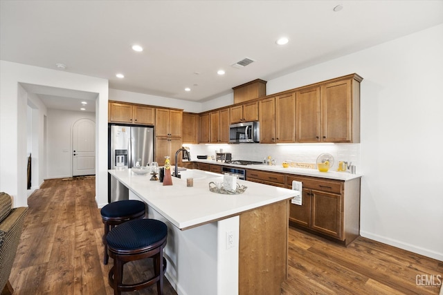 kitchen featuring a center island with sink, appliances with stainless steel finishes, dark hardwood / wood-style flooring, and a breakfast bar area