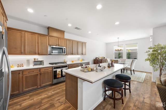 kitchen featuring a center island with sink, stainless steel appliances, hanging light fixtures, a breakfast bar, and dark hardwood / wood-style flooring