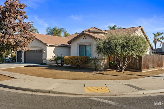 mediterranean / spanish-style house with a tiled roof, a garage, stucco siding, and fence