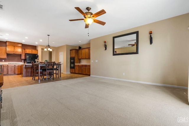 living area featuring light carpet, ceiling fan with notable chandelier, baseboards, and recessed lighting