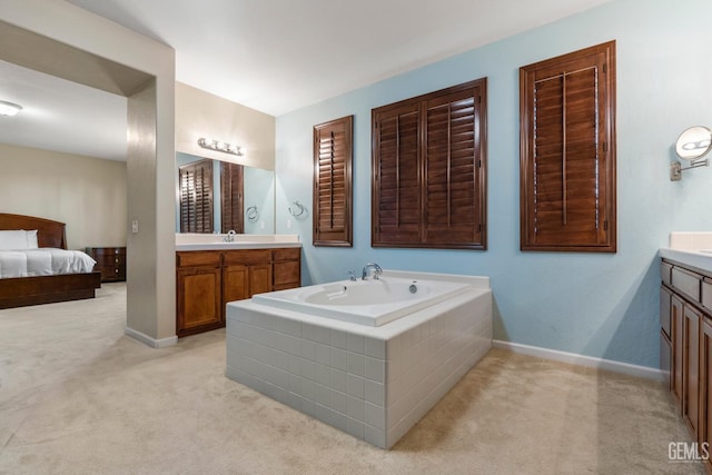 ensuite bathroom featuring a bath, two vanities, a sink, and baseboards
