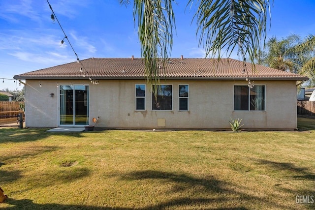 rear view of house featuring stucco siding, fence, a tile roof, and a lawn