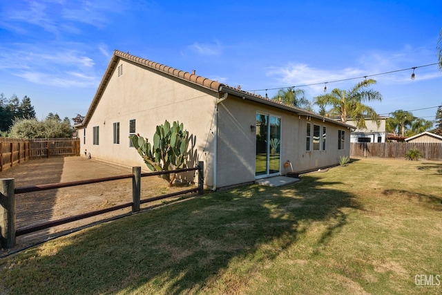rear view of house featuring a fenced backyard, a lawn, and stucco siding