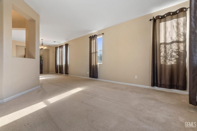 unfurnished room with carpet flooring, baseboards, and an inviting chandelier