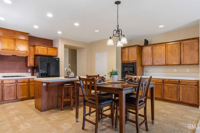 kitchen with a breakfast bar, light countertops, decorative light fixtures, brown cabinets, and black appliances