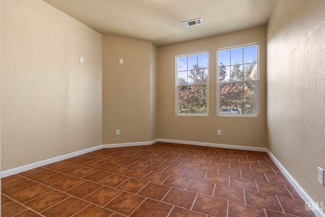 spare room featuring visible vents, baseboards, a textured wall, and a textured ceiling