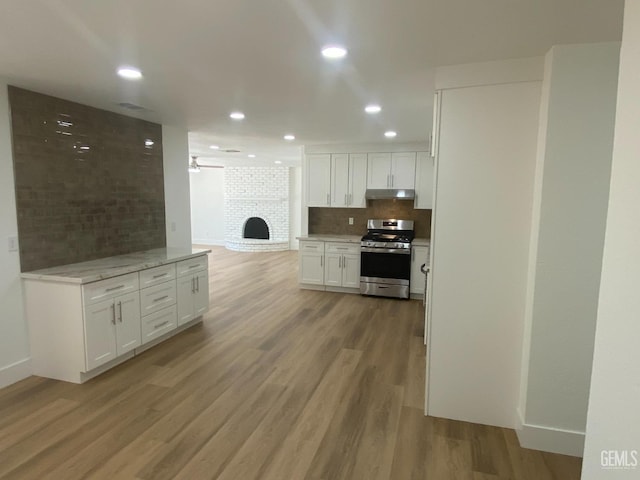 351 Adams St, Wasco, CA 93280 - kitchen with stainless steel gas stove, under cabinet range hood, white cabinets, tasteful backsplash, and light wood-style floors