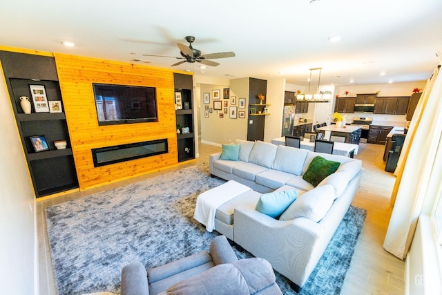 living room featuring wooden walls, ceiling fan with notable chandelier, and light wood-type flooring