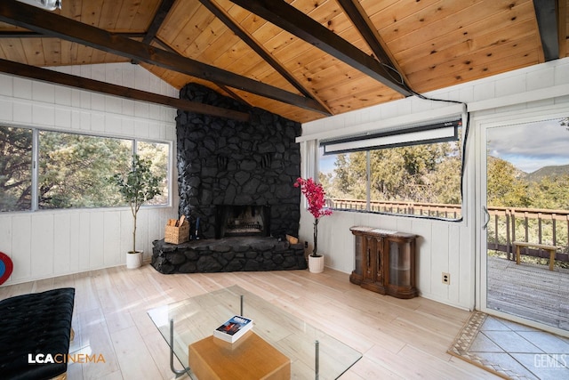 living area featuring a stone fireplace, vaulted ceiling with beams, wood finished floors, and a wealth of natural light