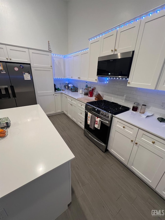 kitchen featuring white cabinets, appliances with stainless steel finishes, dark hardwood / wood-style flooring, and backsplash