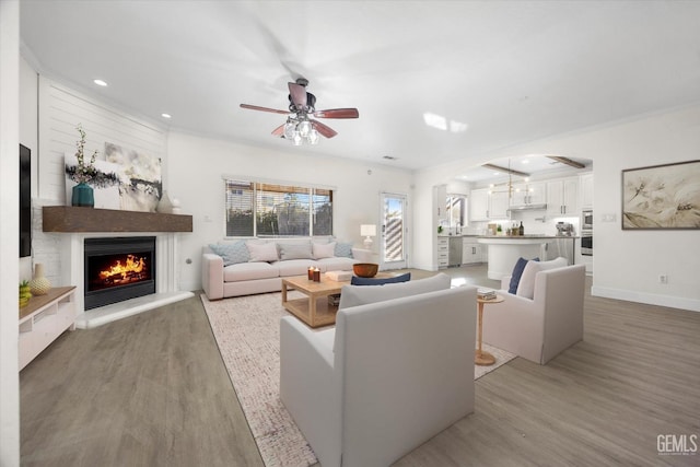 living room featuring ceiling fan, a large fireplace, crown molding, and light hardwood / wood-style floors