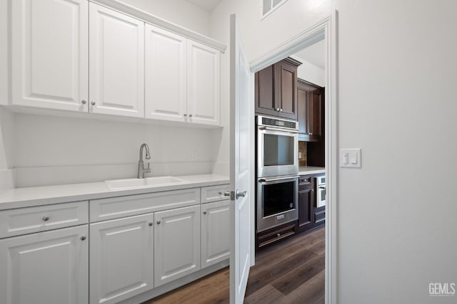 kitchen with white cabinets, double oven, dark wood-type flooring, and sink