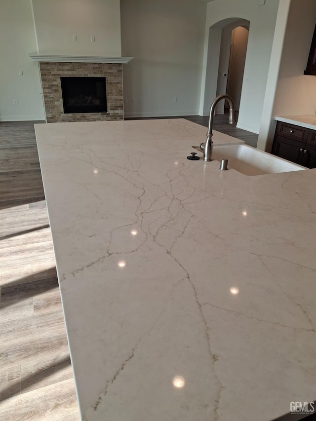 kitchen featuring light stone countertops, sink, dark brown cabinetry, and a stone fireplace