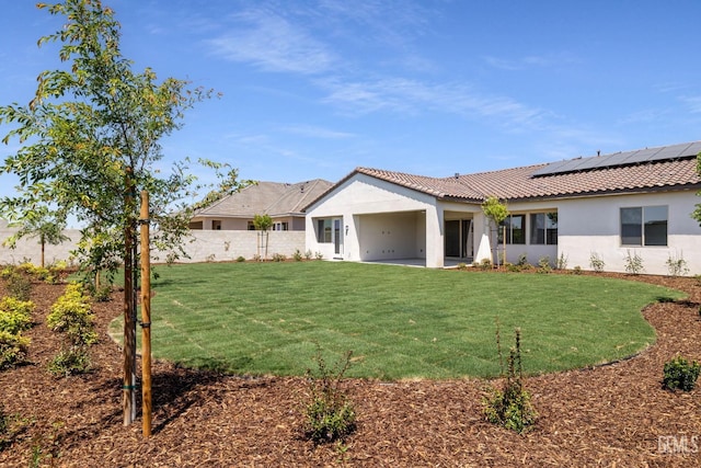 back of property featuring a lawn, solar panels, stucco siding, and a patio area